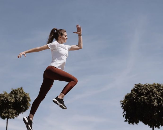 Athletic woman in action jump against a blue sky background. Captures fitness in motion.