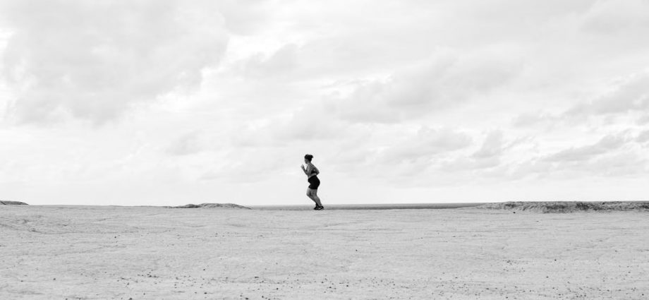 Black and white photo of a lone person running on a vast barren landscape in Natal, Brazil.